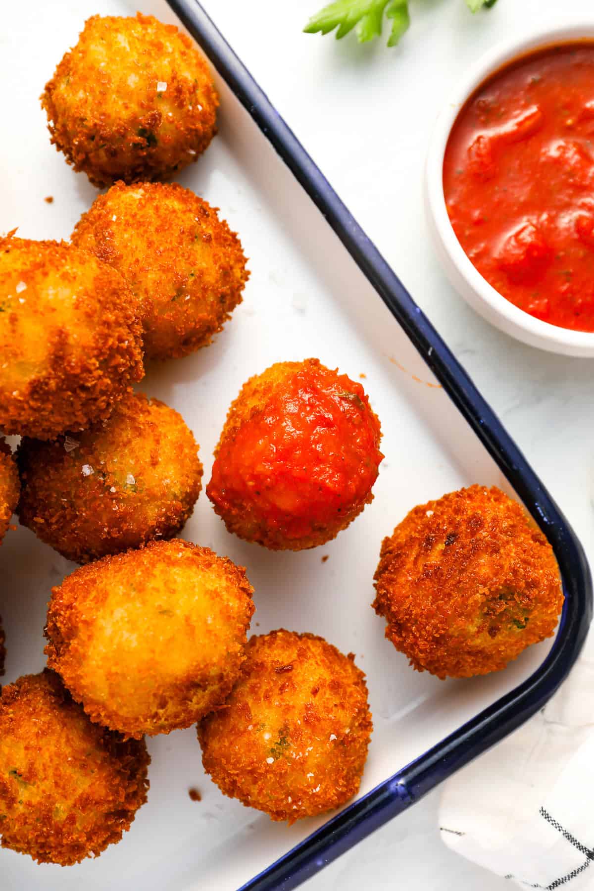 arancini dipped in tomato sauce on a metal tray.