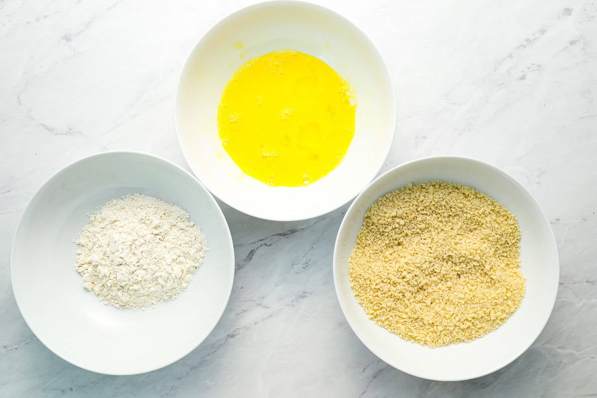 a bowl full of flour, a bowl full of eggs, and a bowl full of breadcrumbs.
