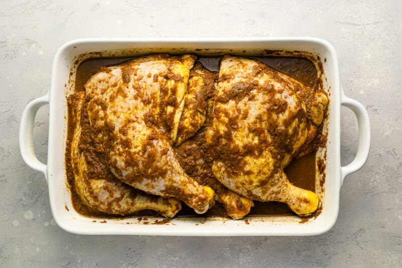 chicken leg quarters topped with jerk marinade in a baking pan.