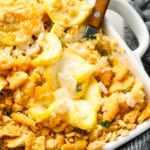 a wooden spoon lifting a scoop of squash casserole from a baking dish.