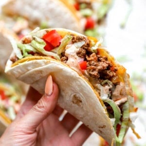 hand holding taco with ground meat, lettuce, tomatoes and taco sauce