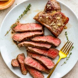 sliced new york strip steak on a white plate with a gold fork