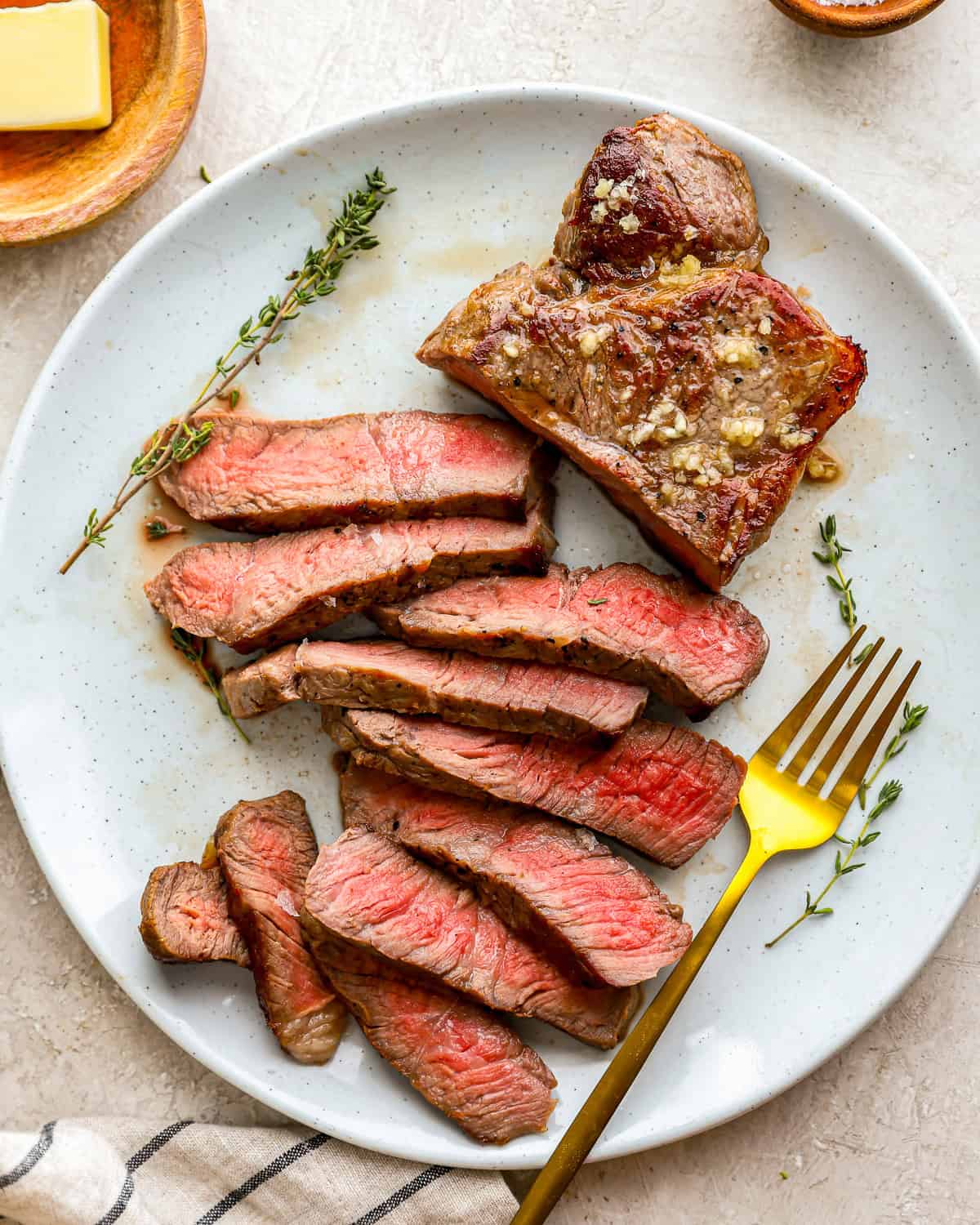 sliced sous vide steak on a white plate with a gold fork and striped towel at the bottom
