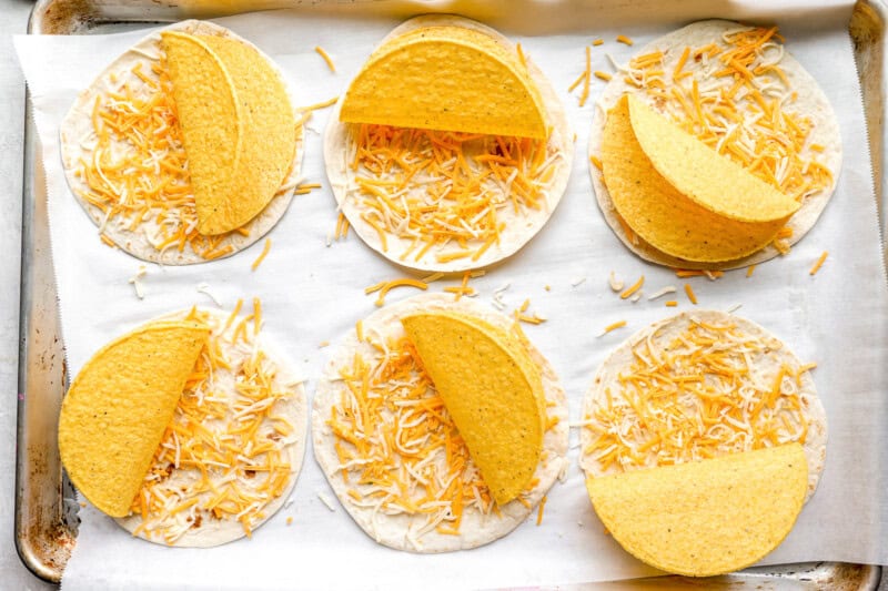 flour tortillas topped with shredded cheese and hard taco shells on a lined baking sheet