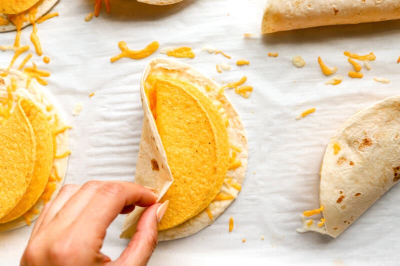 a hand folding a soft tortilla over and hard taco shell