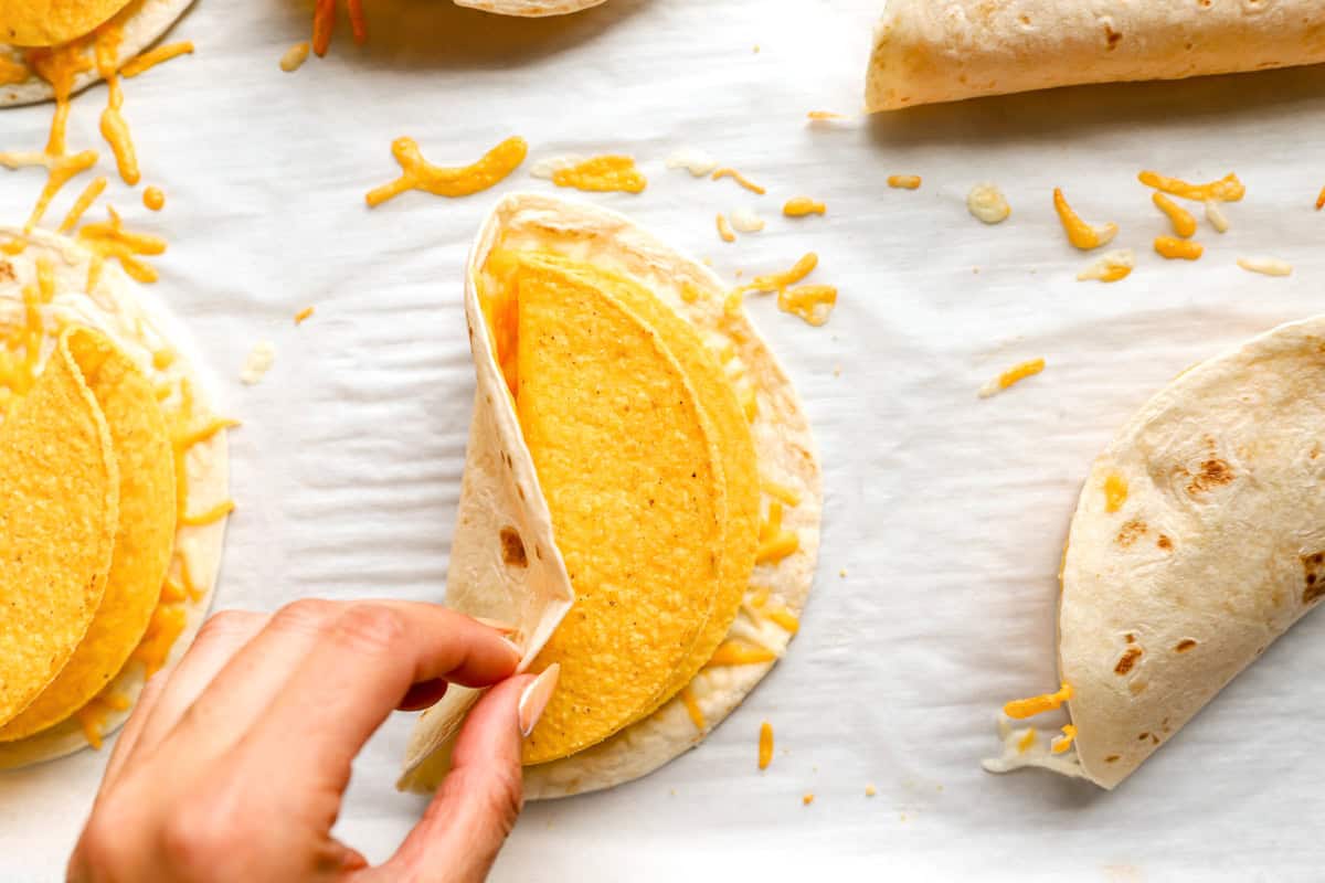 a hand folding a soft tortilla over and hard taco shell