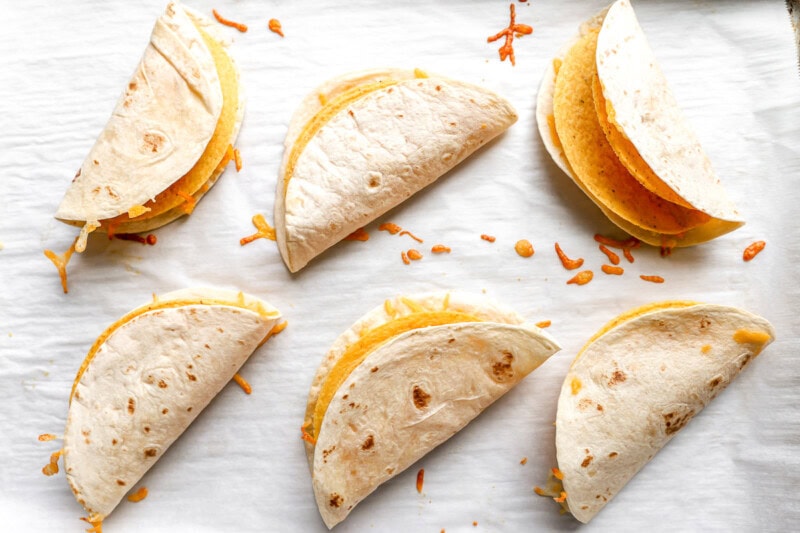 a bunch of hard taco shells covered with flour tortillas laid on a lined baking sheet