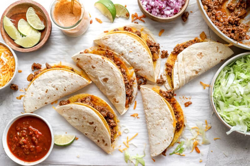 a bunch of ground beef and cheese tacos laid out on a white surface