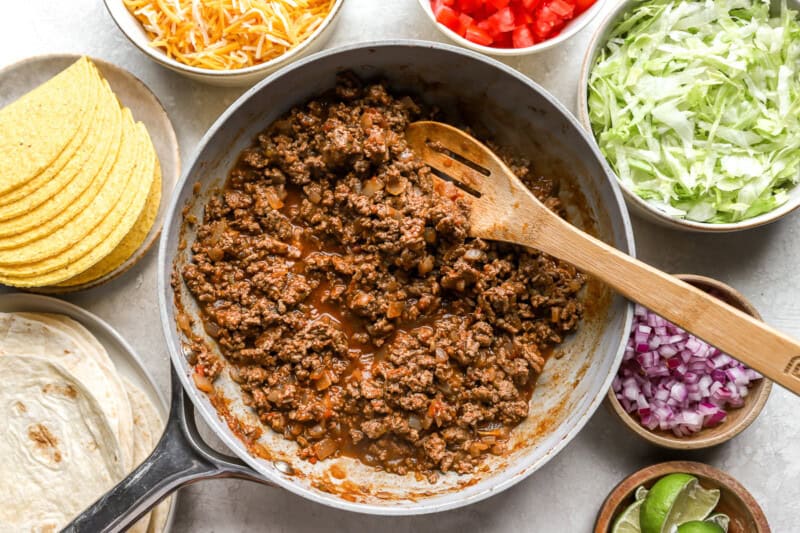 ground beef cooking in cast iron pan with wooden spoon