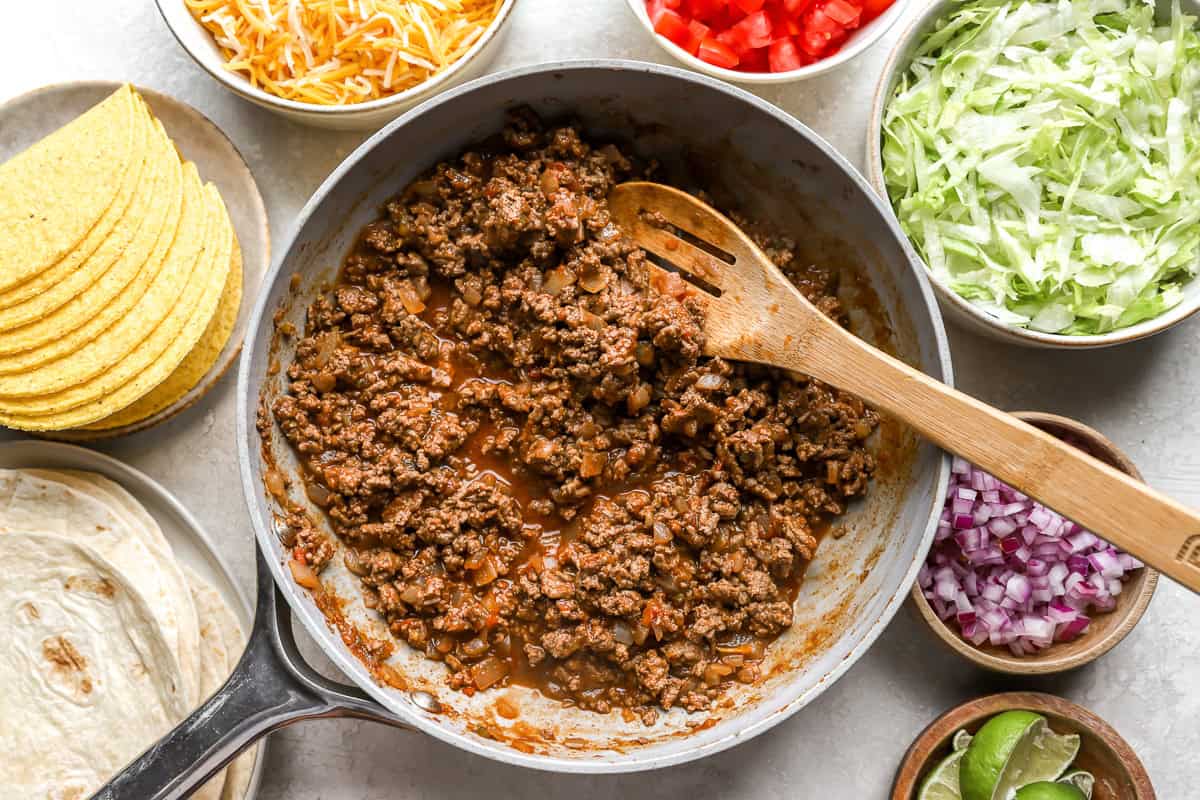ground beef cooking in cast iron pan with wooden spoon