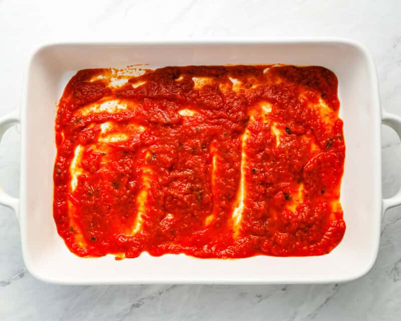 marinara sauce on bottom of white baking dish
