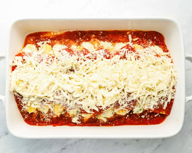 manicotti in white baking dish topped with marinara and shredded cheese