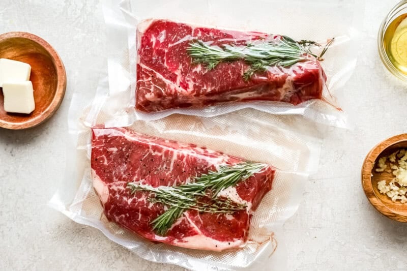 2 new york strip steaks in vacuum sealed bags with rosemary sprigs