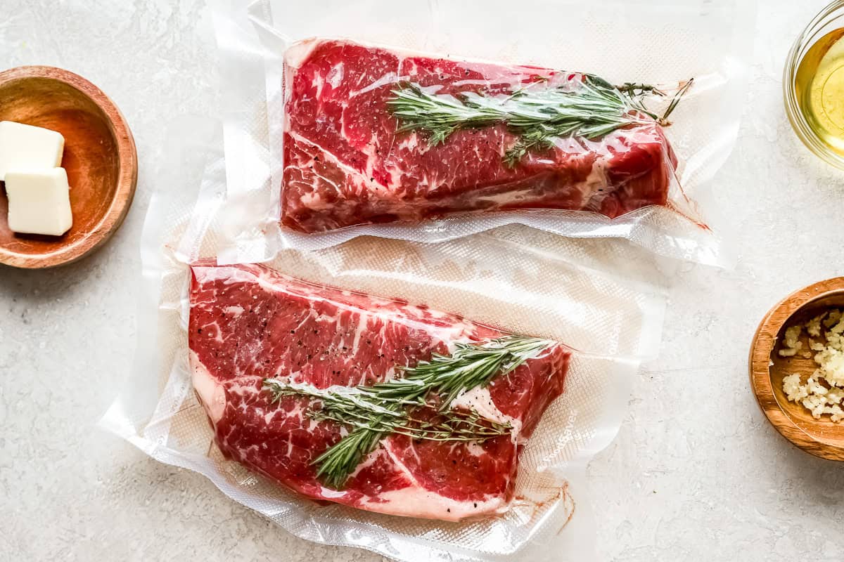 2 new york strip steaks in vacuum sealed bags with rosemary sprigs