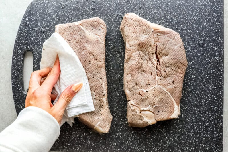 2 sous vide new york steak strips being pat down with paper towel