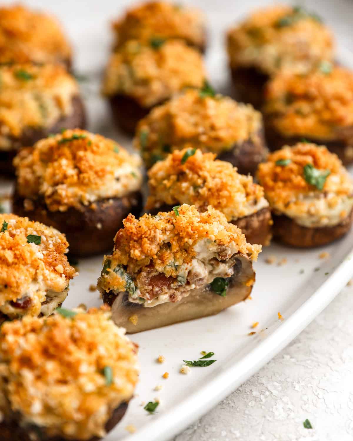 closeup view of a halved bacon stuffed mushroom on a white oval platter with more whole mushrooms.
