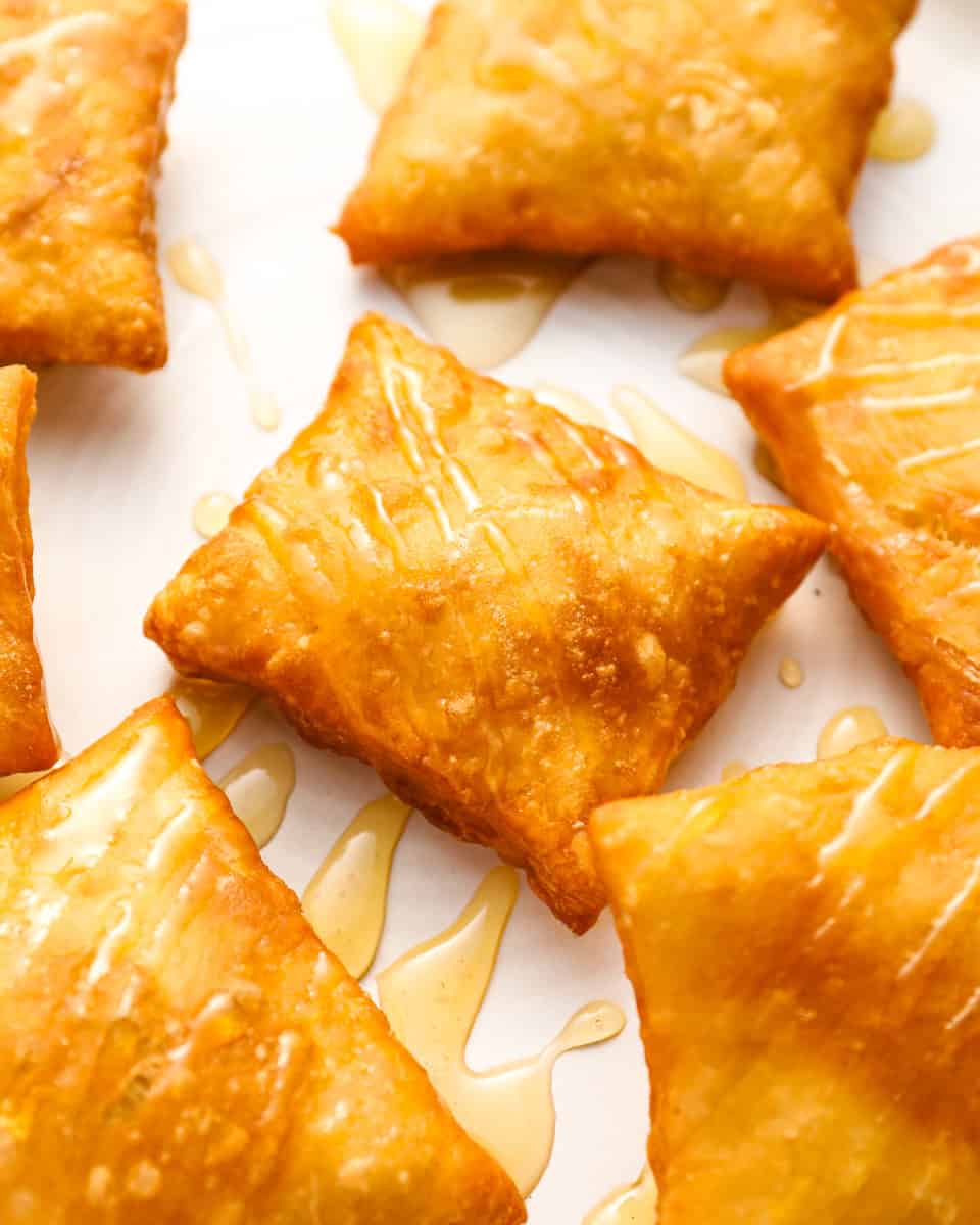 Golden, fried sopapillas drizzled with honey on a white plate, showcasing their puffy and crispy texture.