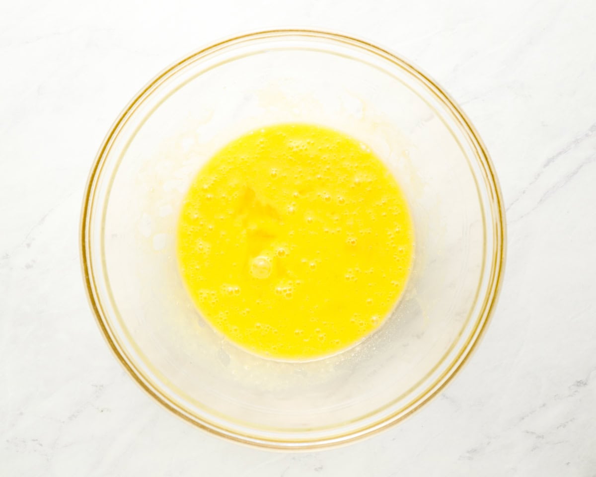A glass bowl containing a beaten egg mixture, prepared as part of the matzo ball dough.