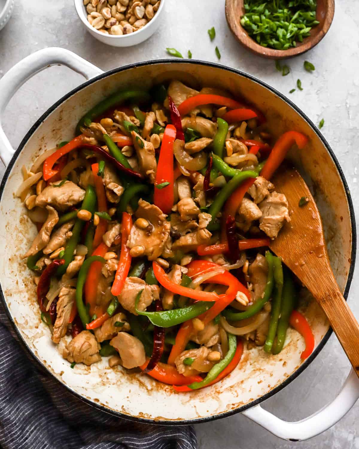 A colorful skillet of Szechuan chicken with vibrant vegetables, peanuts, and a wooden spatula, ready to serve.