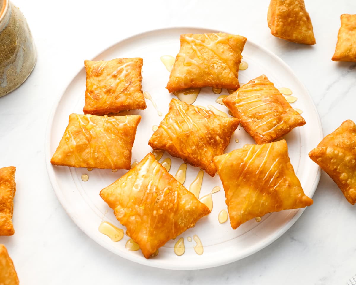 A plate of sopapillas drizzled with honey, arranged neatly, highlighting their puffy texture and golden color.