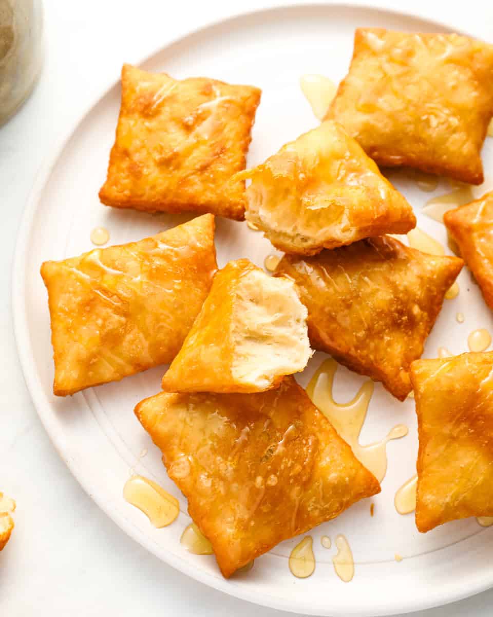 A plate of sopapillas with one torn open, revealing the airy and hollow inside, drizzled with honey.