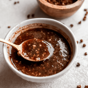 A small bowl of homemade Szechuan sauce on a light surface, with red pepper flakes scattered around for a rustic presentation.