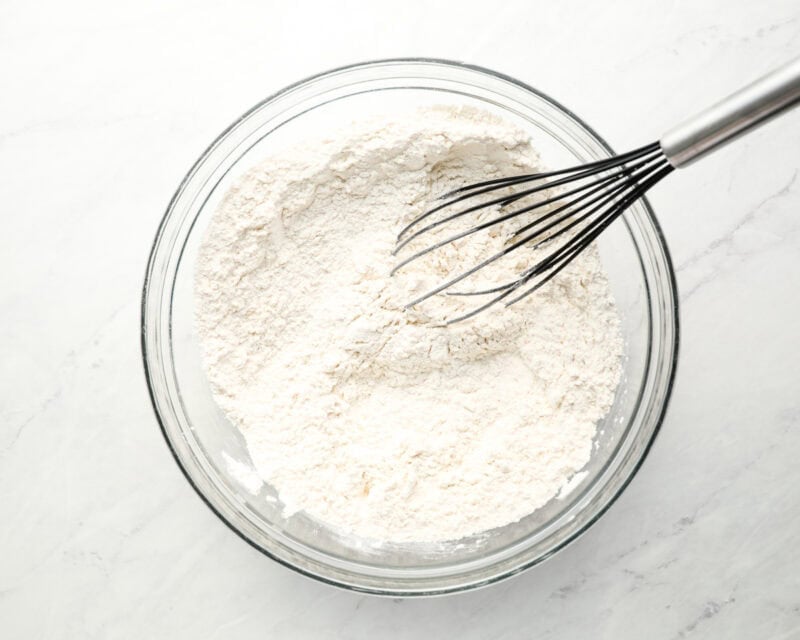 A glass bowl filled with flour and a whisk, showing the beginning stage of the sopapilla dough preparation.