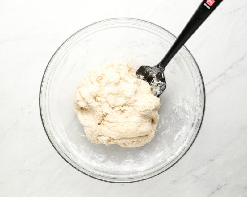 A glass bowl containing freshly mixed sopapilla dough with a black spatula.