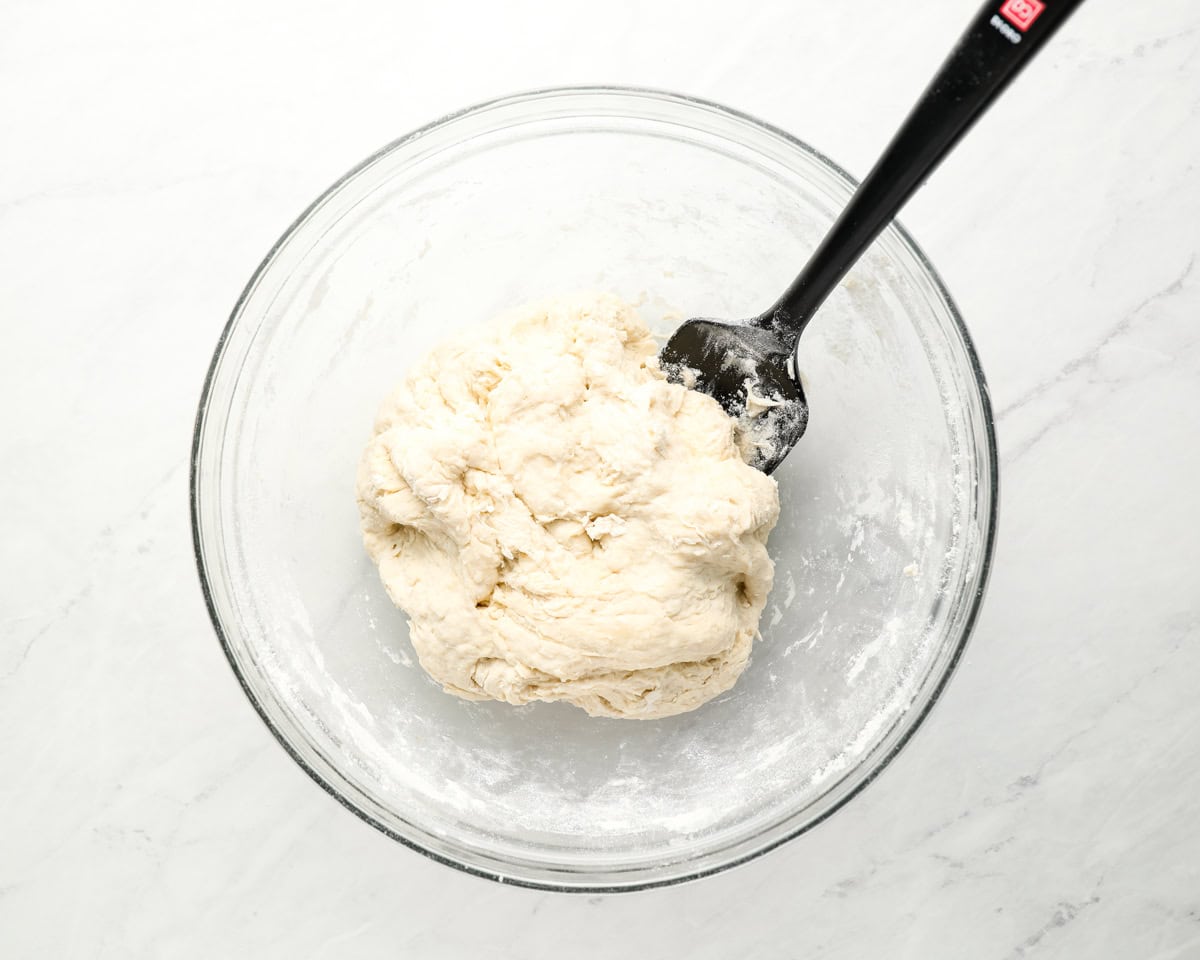 A glass bowl containing freshly mixed sopapilla dough with a black spatula.