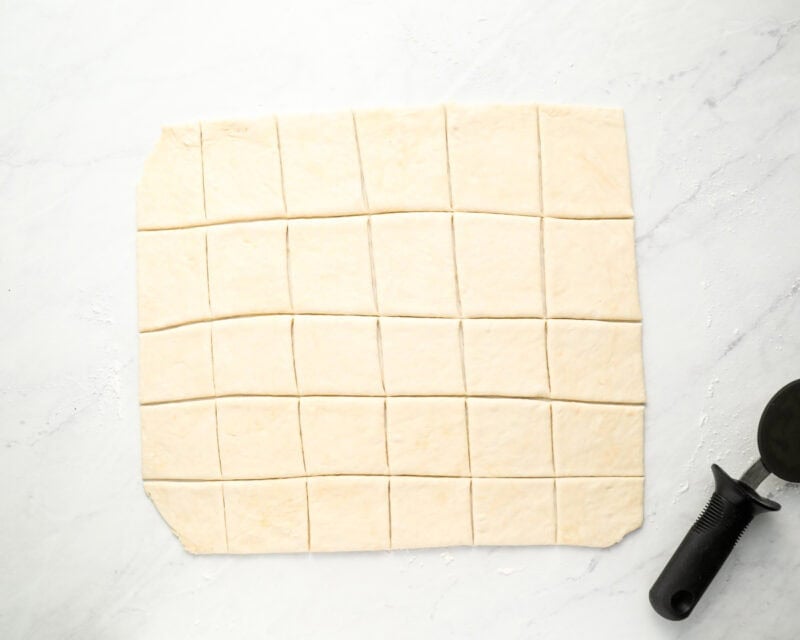 Rolled-out dough cut into squares, prepared for frying, with a dough cutter visible on the side.