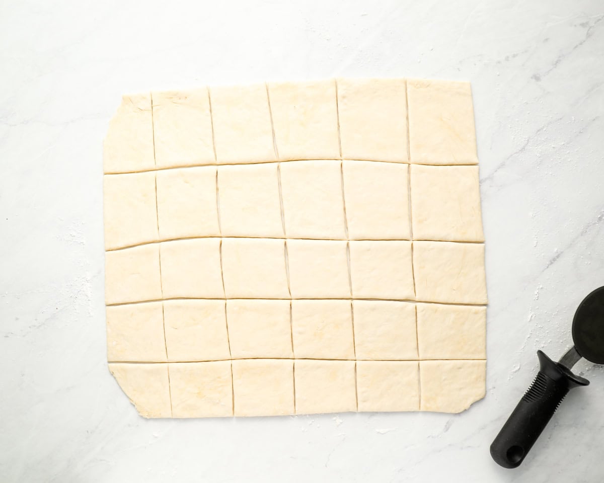 Rolled-out dough cut into squares, prepared for frying, with a dough cutter visible on the side.
