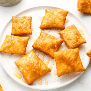 A plate full of fried sopapillas, arranged neatly and drizzled with honey, emphasizing their golden-brown color.