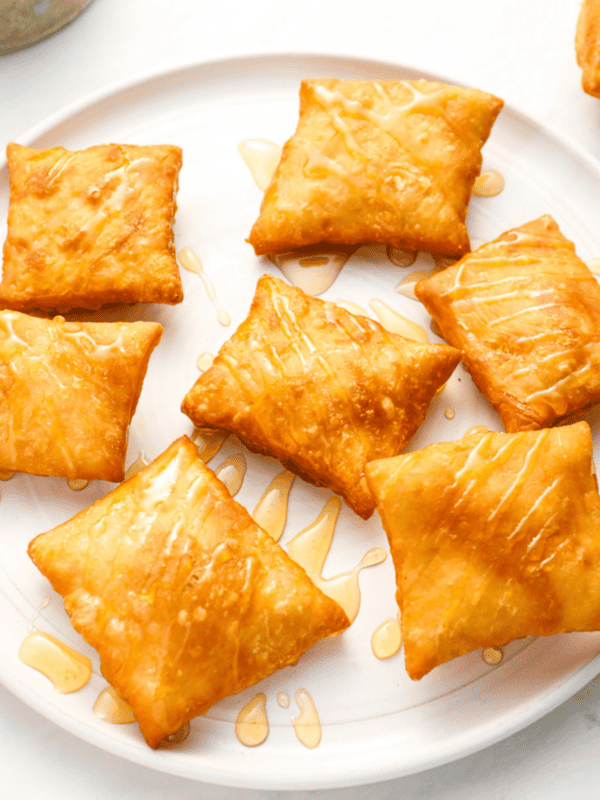 A plate full of fried sopapillas, arranged neatly and drizzled with honey, emphasizing their golden-brown color.