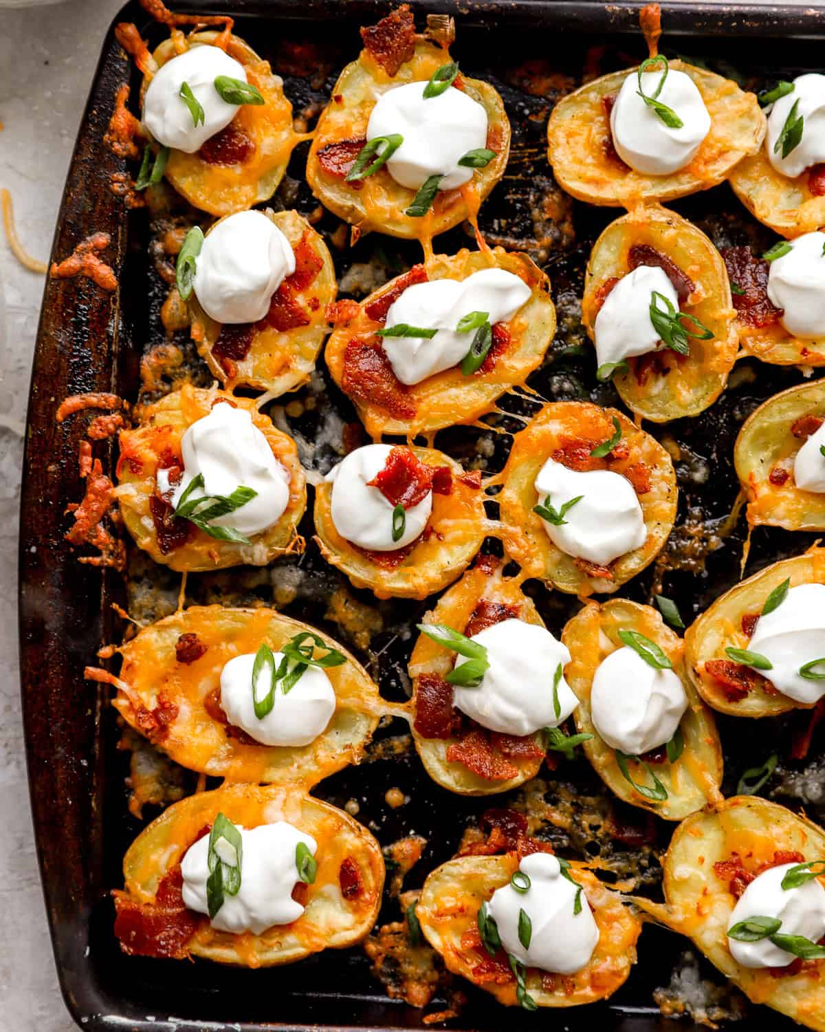 Overhead shot of several loaded potato skin bites grouped together on a pan, with visible melty cheese and dollops of sour cream.