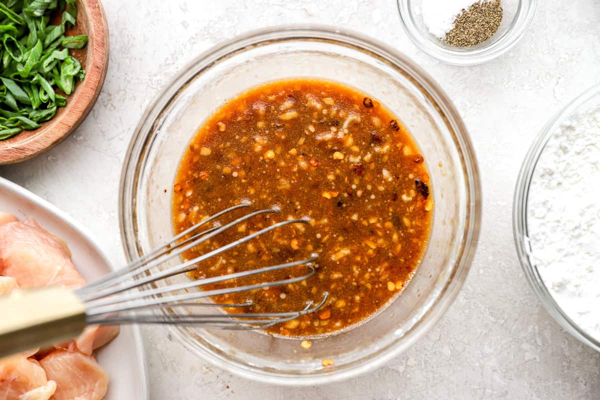 Homemade General Tso’s sauce with garlic, ginger, and chili flakes being whisked in a glass bowl, surrounded by fresh ingredients.