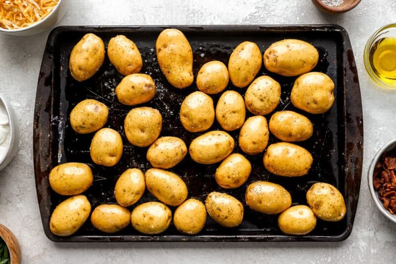 Raw baby yellow potatoes coated in olive oil, salt, and pepper, arranged on a baking sheet ready for roasting.