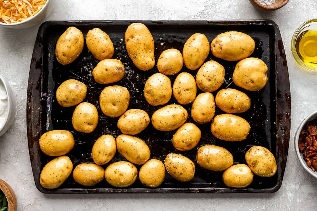 Raw baby yellow potatoes coated in olive oil, salt, and pepper, arranged on a baking sheet ready for roasting.
