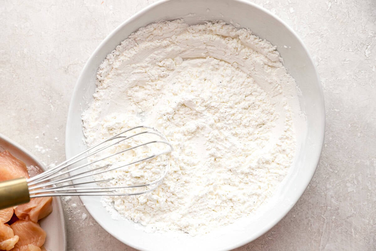 Large white bowl filled with cornstarch, salt, and pepper mixture ready for coating chicken.