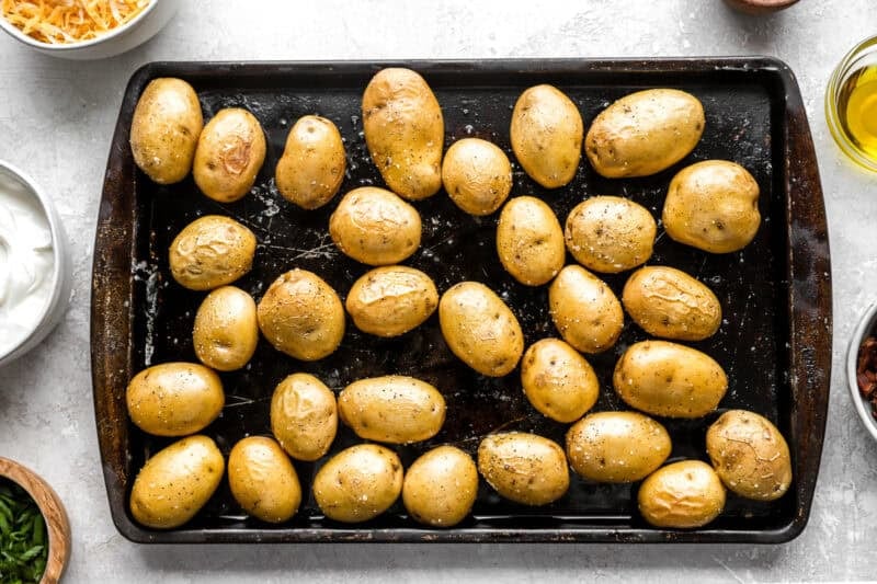 Baby potatoes freshly roasted on a baking tray, showing golden and slightly wrinkled skins after the first bake.