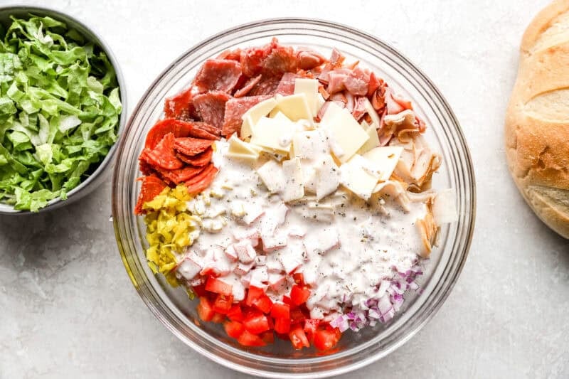 A bowl with chopped meats, cheese, and veggies, with the dressing poured over the top before mixing.
