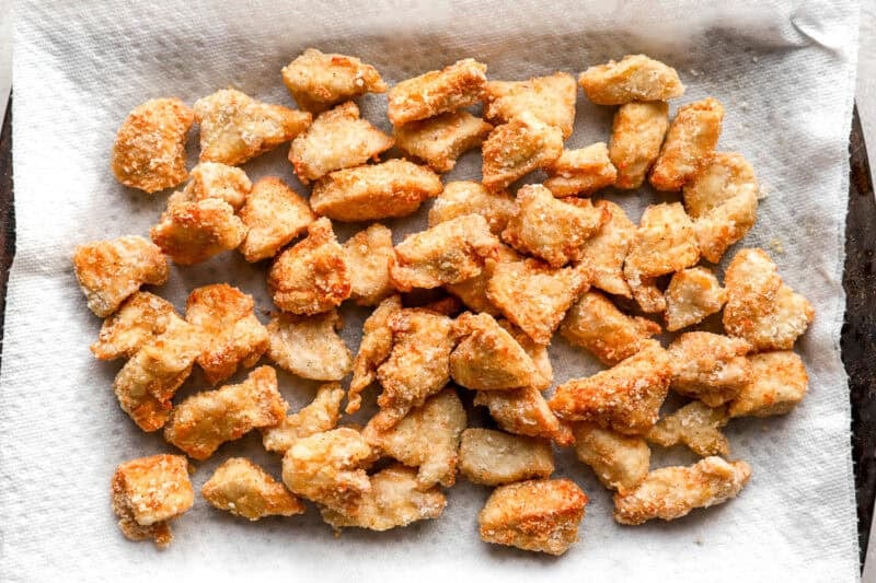 Golden, crispy chicken pieces draining on a paper towel-lined sheet pan after frying.