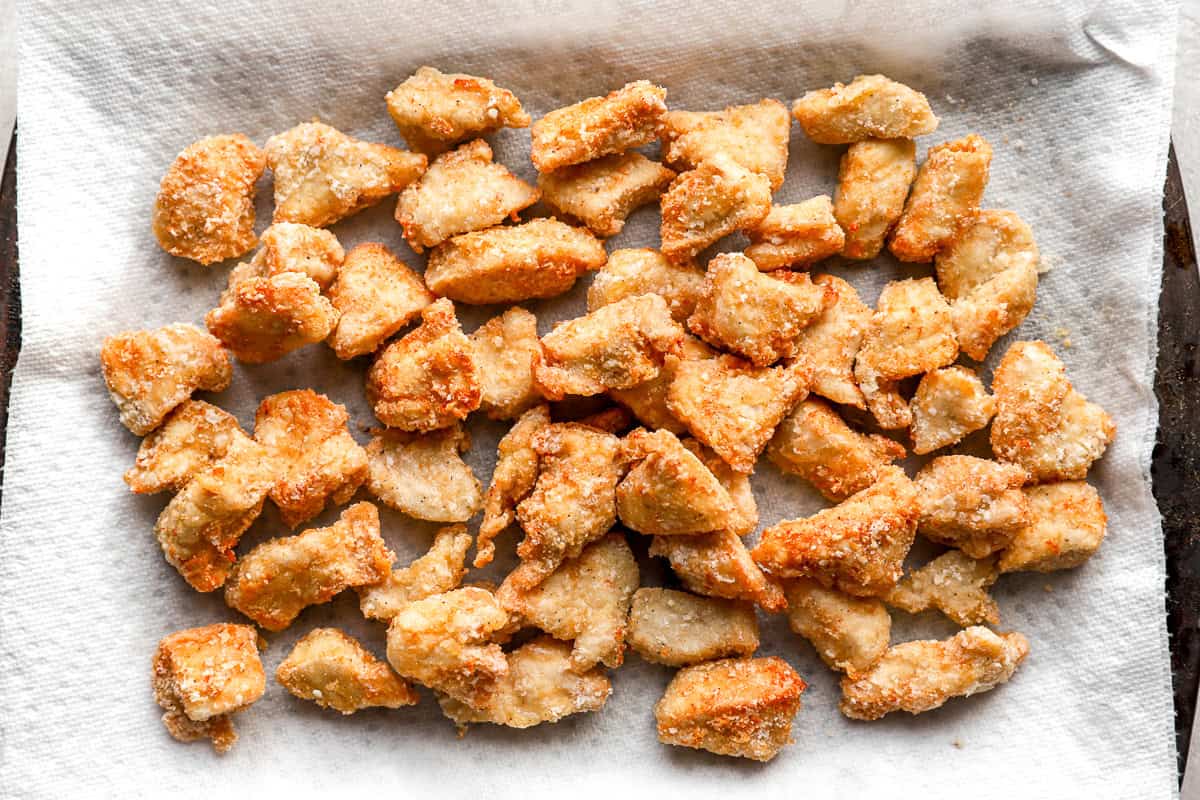 Golden, crispy chicken pieces draining on a paper towel-lined sheet pan after frying.