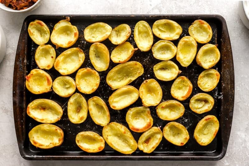 Empty potato skins brushed with oil and baked until lightly golden and crisp, arranged neatly on a dark sheet pan.