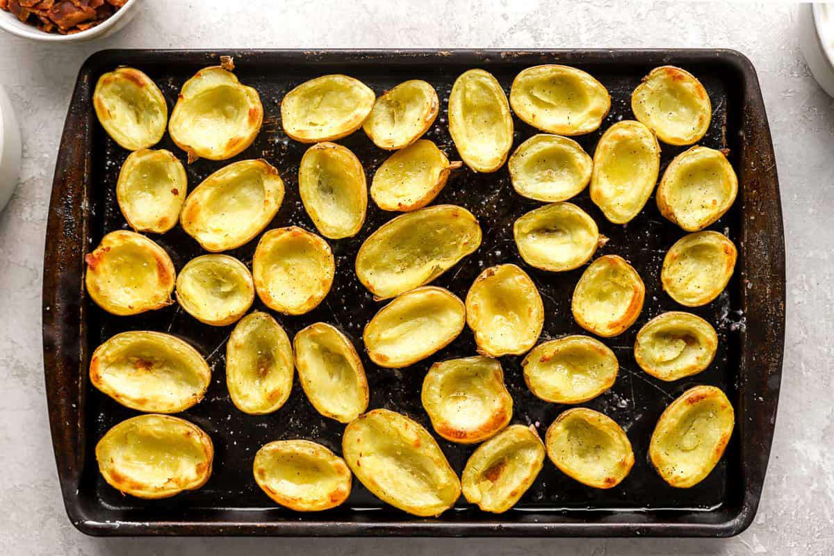 Empty potato skins brushed with oil and baked until lightly golden and crisp, arranged neatly on a dark sheet pan.