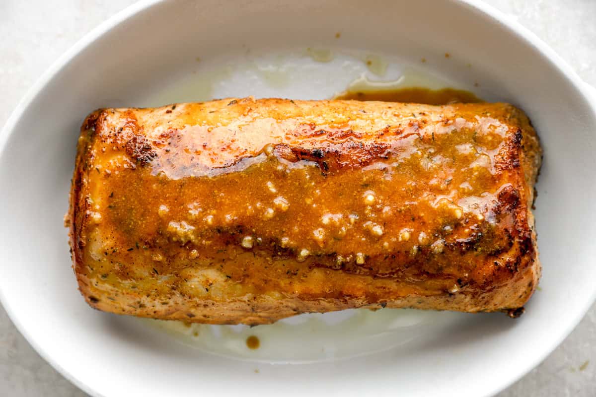 The seared pork loin placed in a white baking dish, coated in the maple Dijon glaze before roasting.
