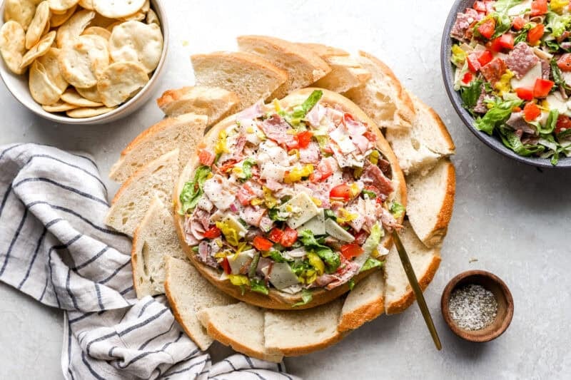 The finished hoagie dip placed in the bread bowl, surrounded by bread slices and crackers for dipping.