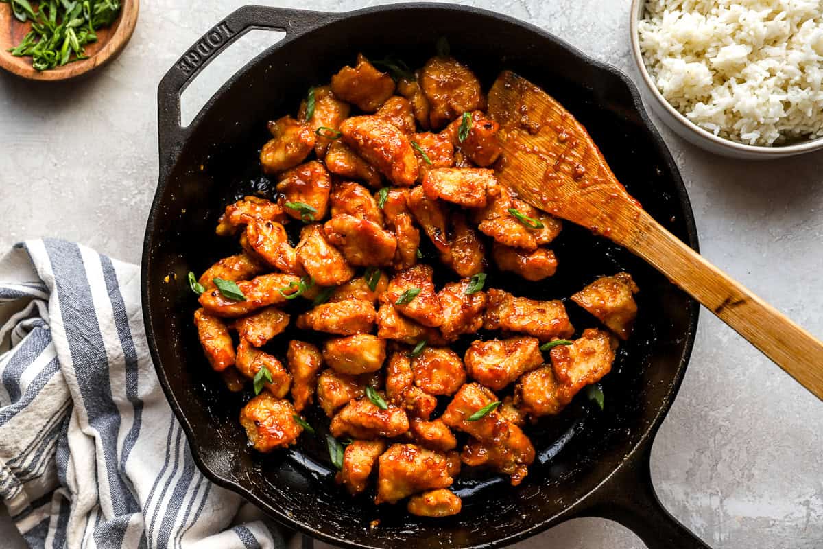 Skillet full of crispy chicken coated in sticky General Tso’s sauce, garnished with green onions.