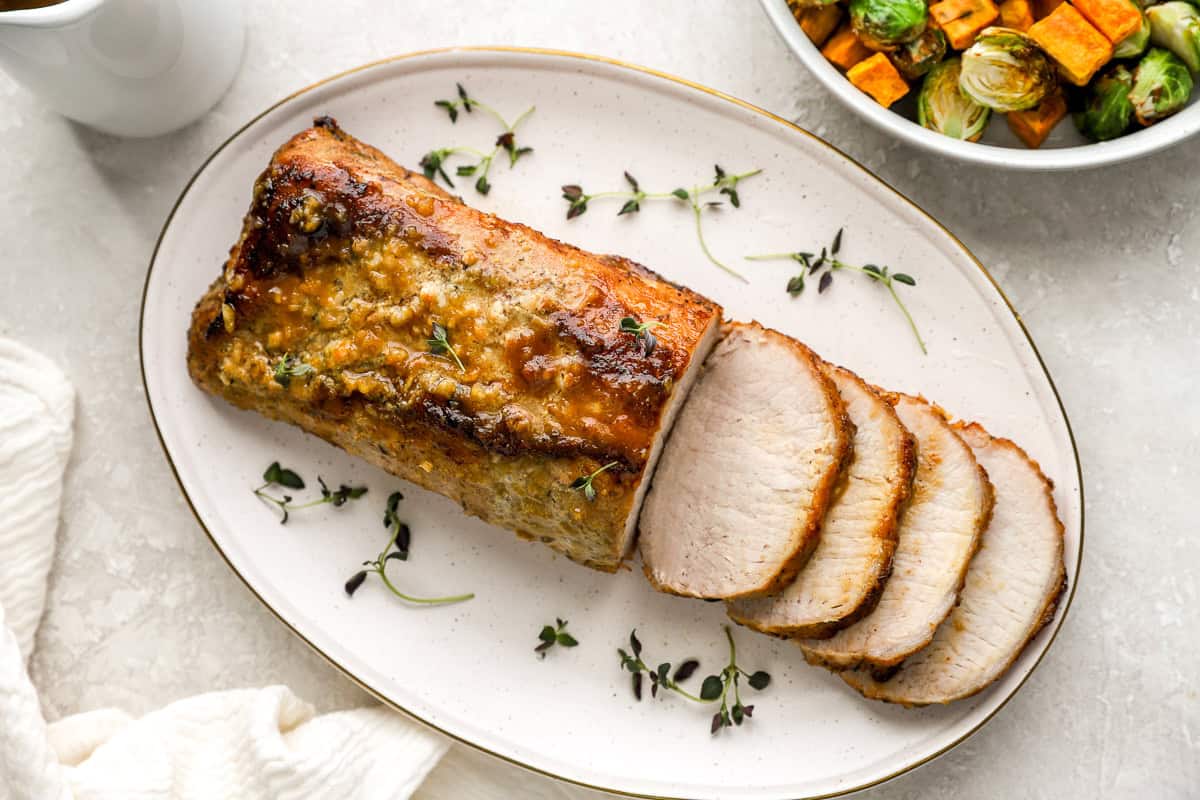 Another view of the sliced roasted pork loin on a serving platter, drizzled with sauce and garnished with fresh thyme, ready to be served.