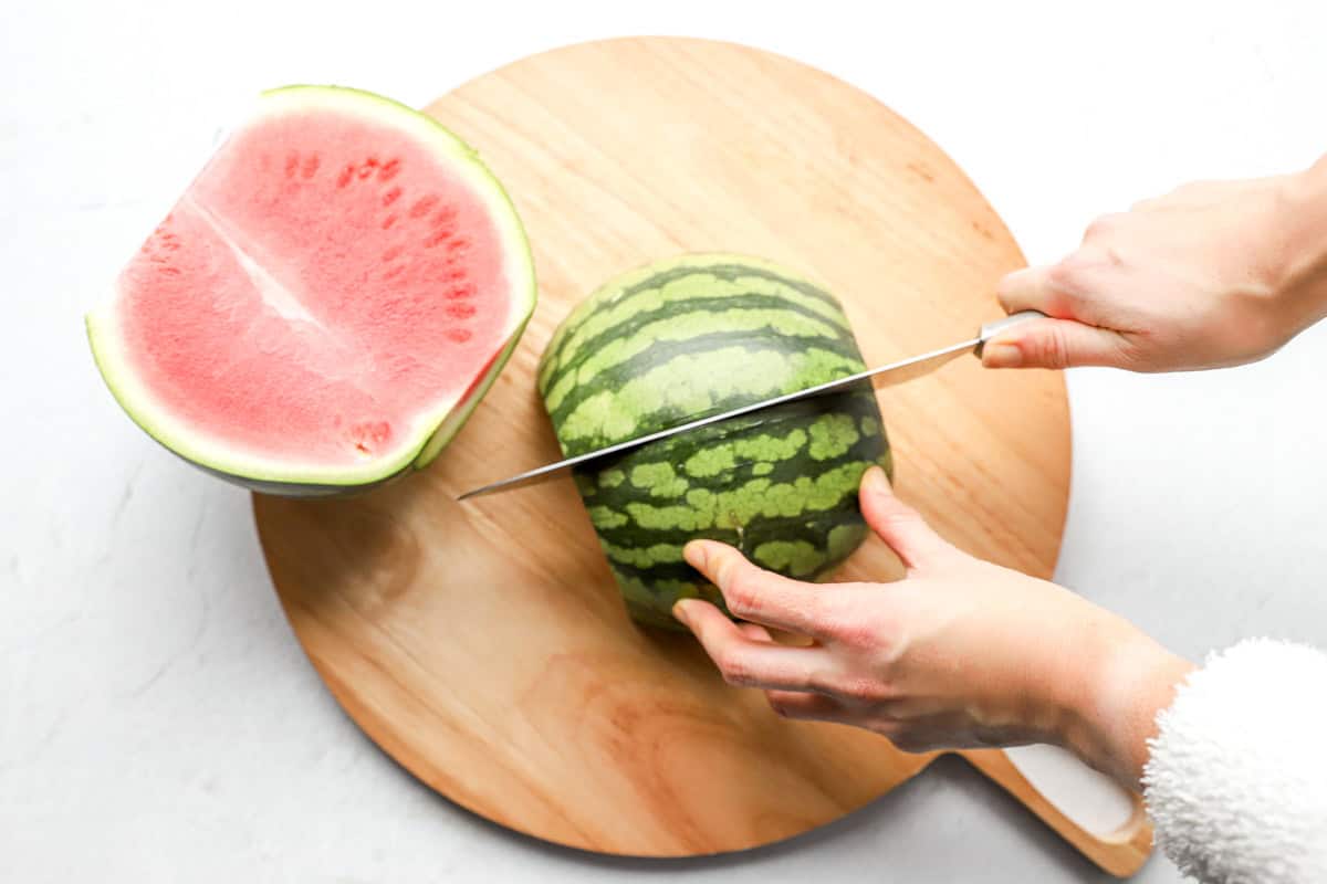 Knife cutting the watermelon in half lengthwise, one half already set aside showing the interior.