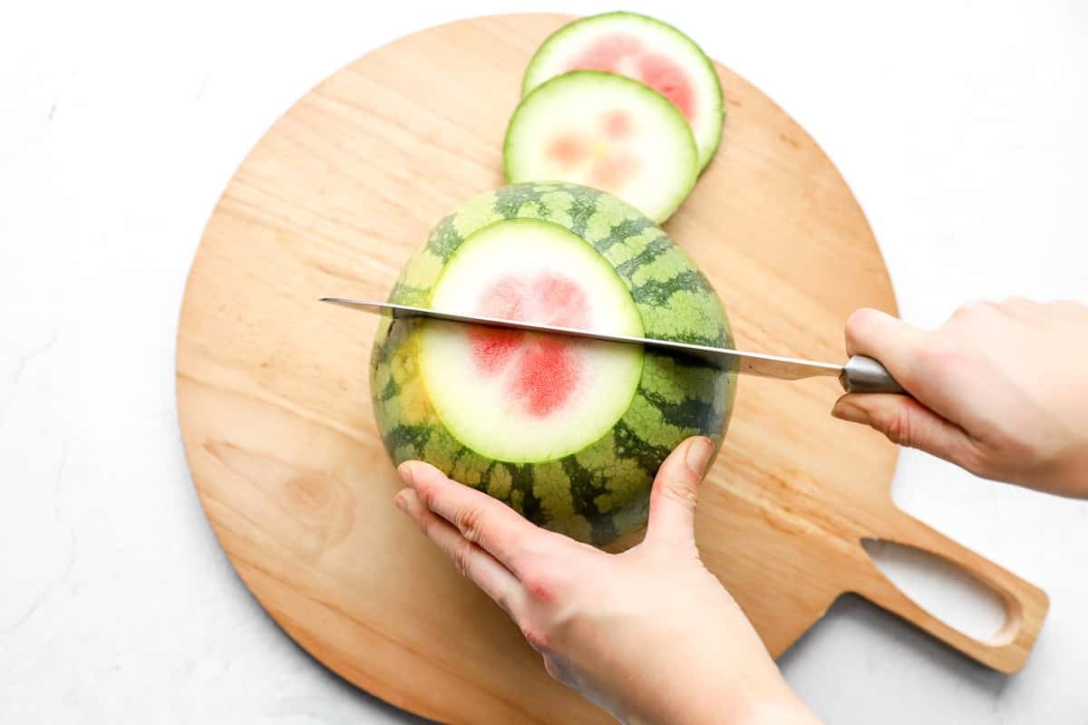 Knife slicing off the bottom end of the watermelon, showing the red center and rind layers.
